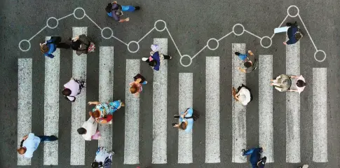An overhead view of a small crowd crossing a street at a crosswalk, representing ALICE. Data markers connecting the crosswalk lines symbolize the latest State of ALICE research.